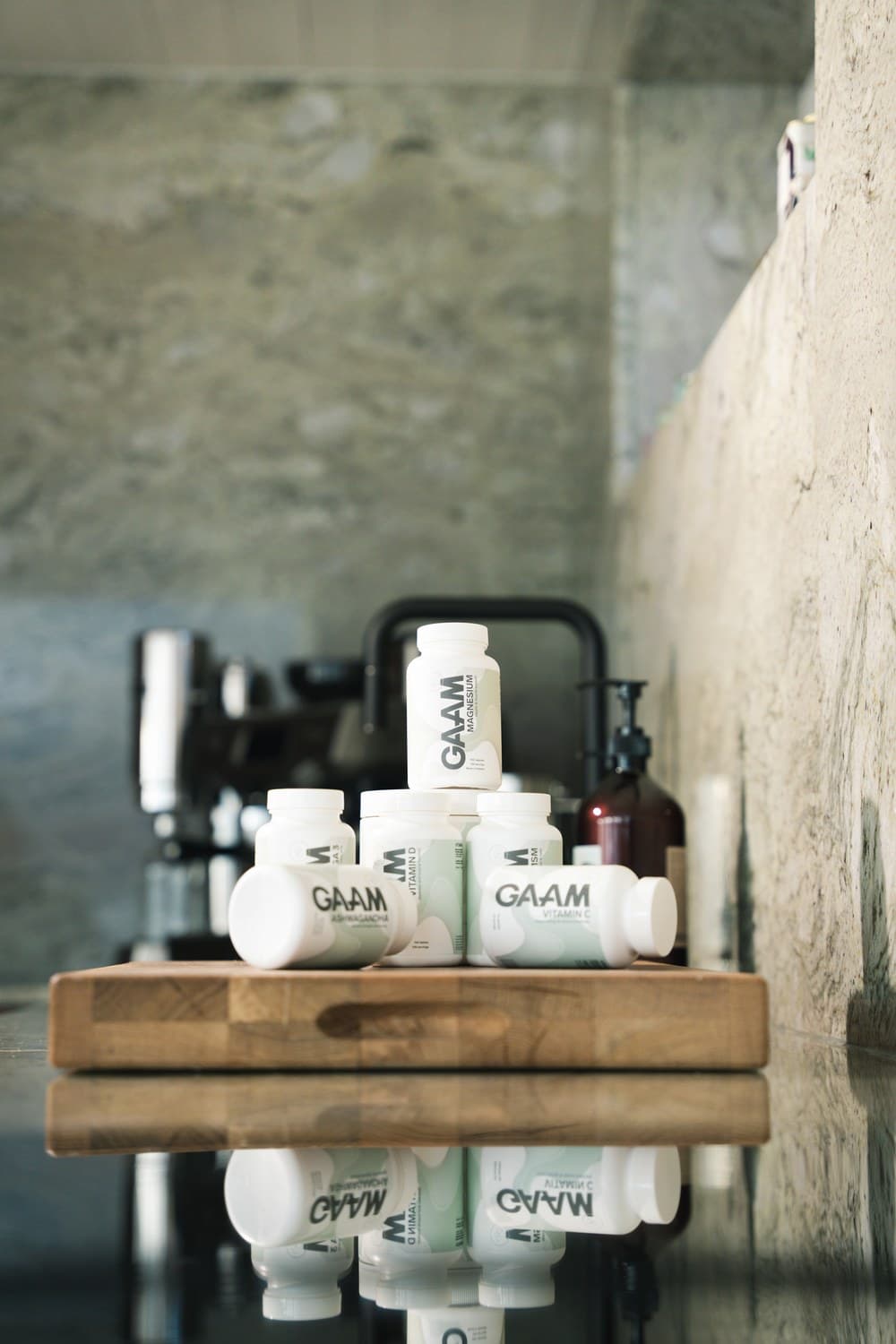 White GAAM supplement and vitamin tubs stacked on a wooden board on a dark stone counter